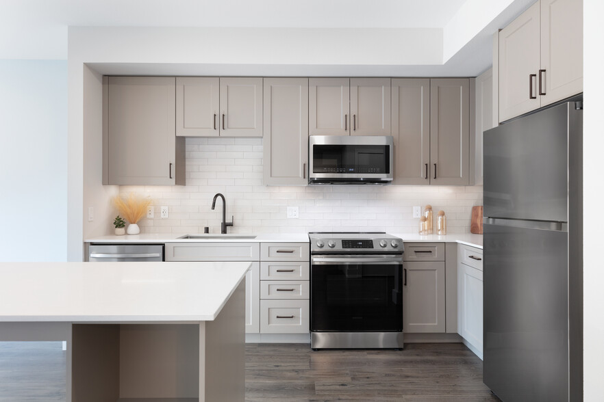 Coming Soon - New West Phase apartments - Finish Package III Kitchen with stainless steel appliances, white quartz countertops, grey cabinetry, pendant lighting, and hard surface flooring (Representative photo) - Avalon Hunt Valley and Hunt Valley West