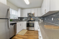 Renovated Package II kitchen with white cabinetry, grey quartz countertops, grey tile backsplash, stainless steel appliances, and hard surface plank flooring throughout common areas. Soft-close cabinets and microwaves available in select homes - eaves Wilmington and Wilmington West