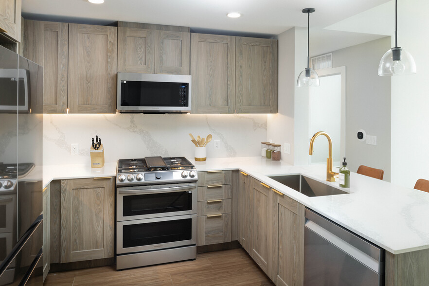 Signature Collection kitchen with stainless steel appliances, marbled white quartz countertops, brown cabinetry, and hard surface flooring - Avalon Montville