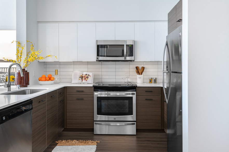 Apartment kitchen with stainless steel appliances, quartz countertops and wood-style flooring. - Griffis Lake Washington