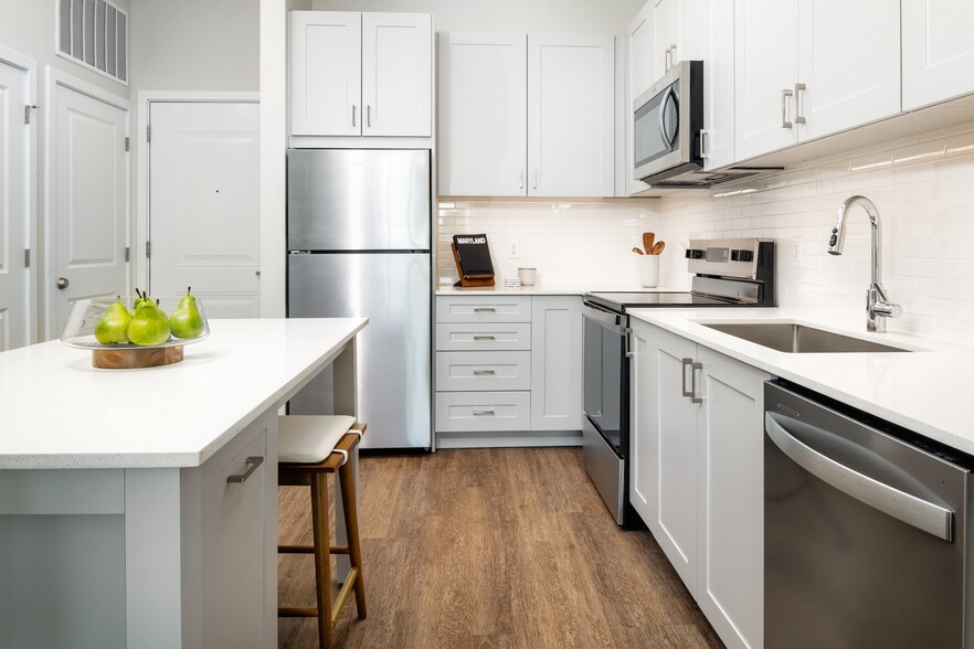 New West Phase - Finish Package III Kitchen with stainless steel appliances, white quartz countertops, grey cabinetry, and hard surface flooring - Avalon Hunt Valley and Hunt Valley West