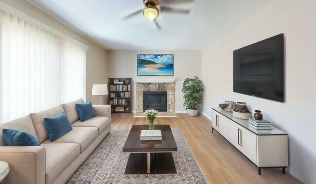 Bright and elegant living room featuring a plush beige sofa, a cozy stone fireplace, and a large wall-mounted TV. - Villas of Stone Ridge