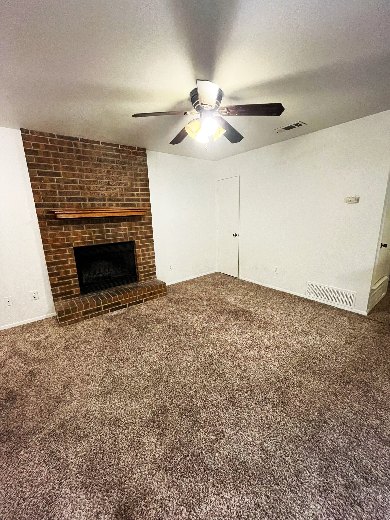 Cozy, living room featuring a warm brick fireplace with mantel, ceiling fan, plush carpet and closet - 4917 Jamesway Rd