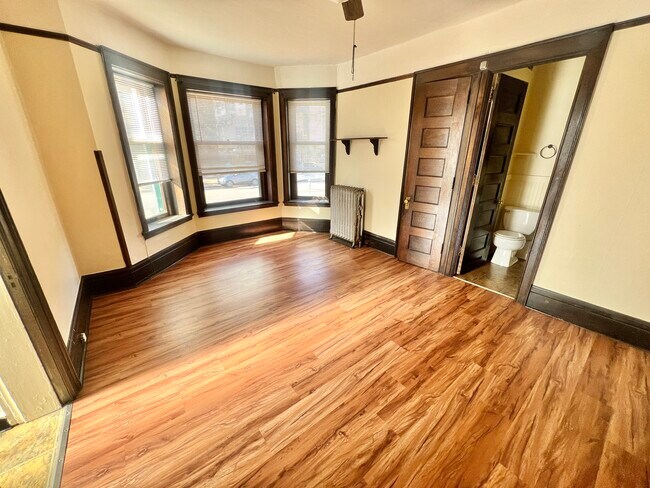 Step into this sunlit space with beautiful wood floors and easy access to a private bathroom, perfect for relaxation. - Cross Apartments