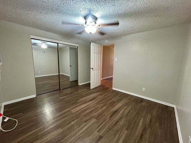 Spacious bedroom with elegant wood flooring, mirrored closet doors, and modern ceiling fan for a cozy atmosphere. - Boardwalk Apartments