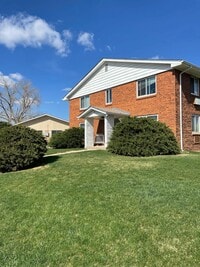 Inviting brick apartment building with manicured lawn and bright windows under a clear blue sky. - Allison West Apartments