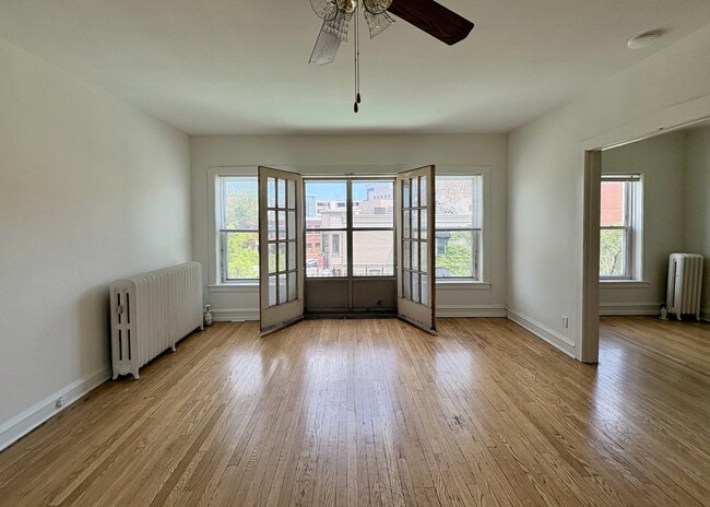 Bright and airy living space with wooden floors, large windows, and elegant French doors offering a charming view of the neighborhood. - Ivanhoe