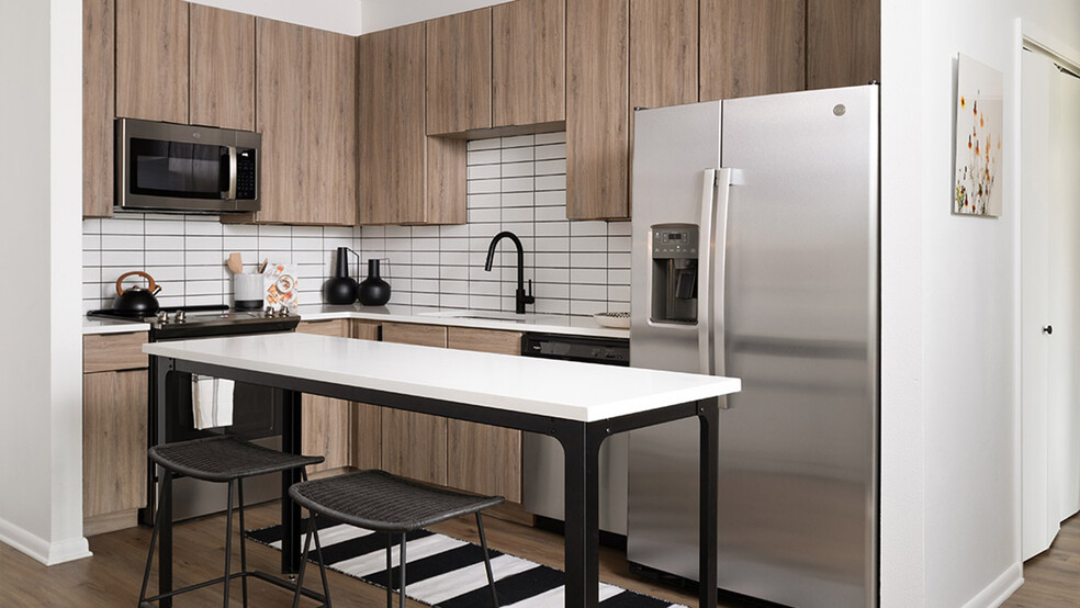 Apartment kitchen with stainless steel appliances, quartz countertops and wood-style flooring. - Griffis at The Domain