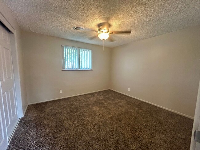 Inviting bedroom with cozy carpet, a ceiling fan, and ample natural light from a large window. - Boardwalk Apartments
