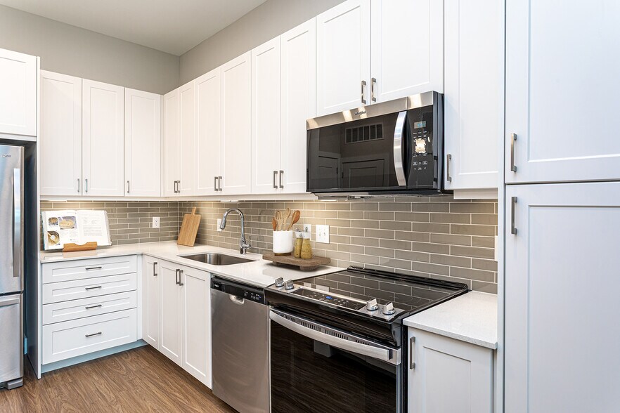 Modern kitchen with white cabinetry, undercabinet lighting, grey tile backsplash, and white quartz countertops - Avalon Carmel Commons