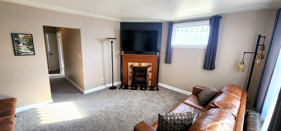 Bright living room with large window, cozy fireplace, and mounted TV - 822 E 4th St