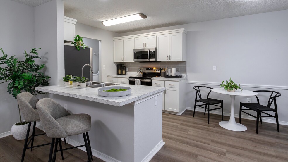 Enjoy the contemporary design of this kitchen featuring a breakfast bar, stainless steel appliances, and a comfortable dining area. - The Avenue