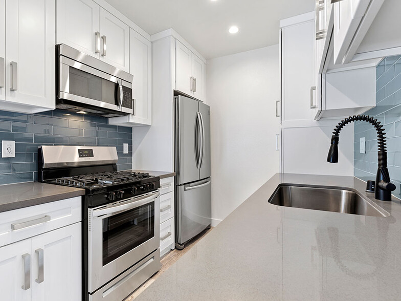 Blue tiled kitchen with quartz stone counters and stainless steel microwave, oven, fridge, and fixtures. - Cedar Glen