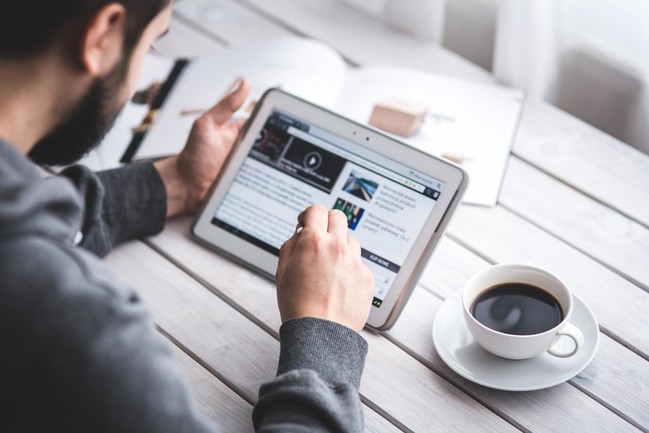 Stock photo of man sitting at table drinking coffee and looking at iPad - The Haven at Indigo Square