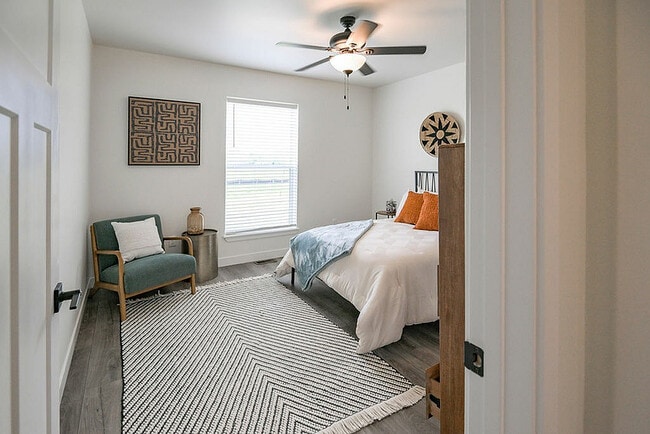 Inviting bedroom with modern decor, featuring a cozy bed with white linens, stylish armchair, and bright window for natural light. - Highland Park Apartments