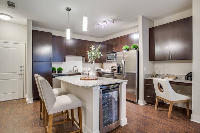 Kitchen with island, granite countertops, dark wood cabinetry, and stainless steel appliances - Park Central at Flower Mound