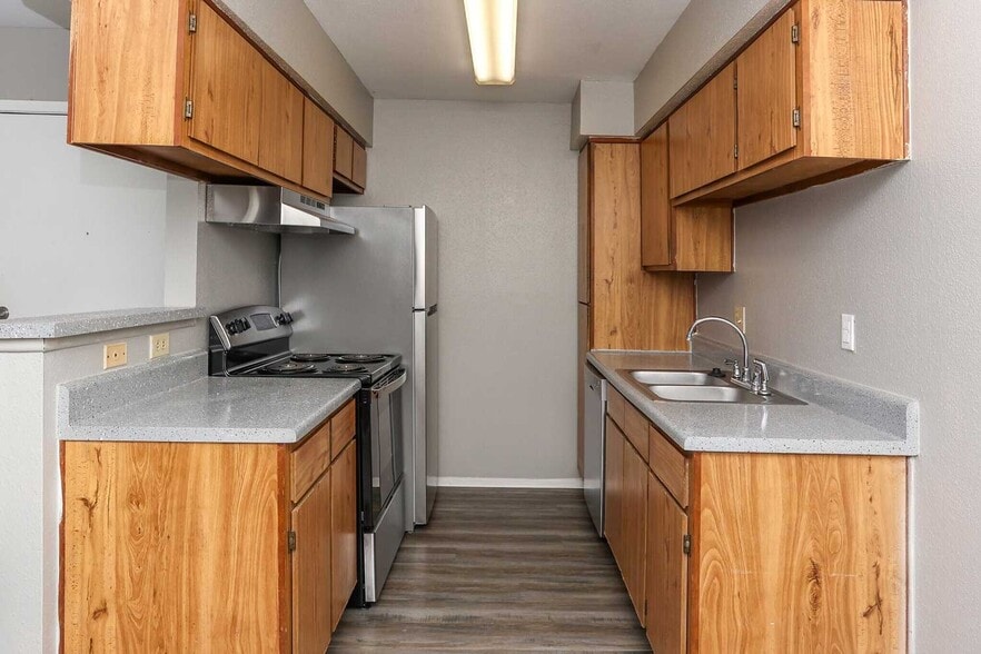 Galley kitchen with wood cabinetry, gray countertops, double sink, electric range, and full size refrigerator - Park at Summerhill