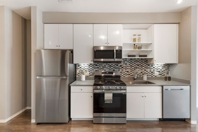 Renovated Package I kitchen with stainless steel appliances, dark quartz countertops, white cabinetry, tile backsplash, and hard surface flooring - AVA Somerville