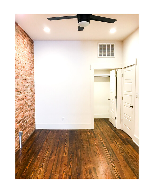 Bedroom with exposed brick, ceiling fan, wall tv hook ups. Toward the back is the walk in closet, through the right door is the bathroom. - 18 W State St