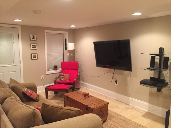 fully-finished Living room with queen-sized sleeper sofa, coffee table with storage, coat hook, rug, secretary desk with storage, arm chair, Minisplit HVAC unit, wall-mounted flat screen smartTV and sound system with speakers, 2 large secure windows, and closet with separate washer and dryer and ... - 43 Girard St. NE