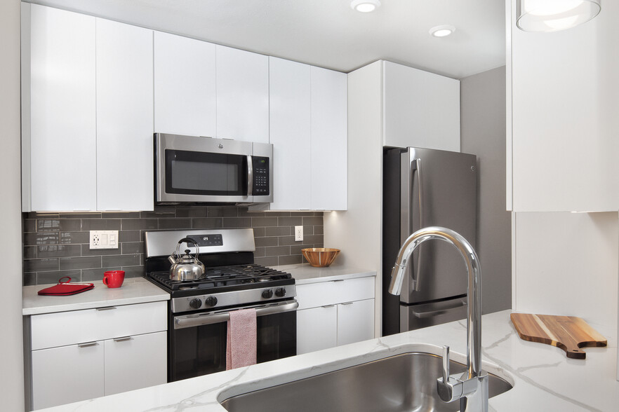 Premier Scheme kitchen with flat white cabinetry, white marbled quartz countertops, grey subway tile backsplash, stainless steel appliances, and hard surface flooring - Avalon Melville