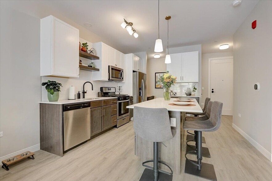 Kitchen with island, stainless steel whirlpool appliances, quartz countertops, floating shelves and two tone cabinets - Lilac Station