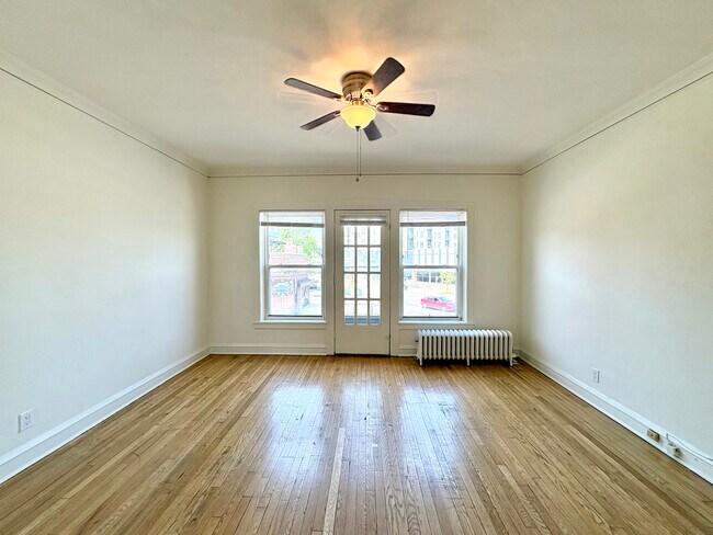 Bright and spacious living room with polished hardwood floors, large windows, and a ceiling fan, offering cozy urban views. - Ivanhoe