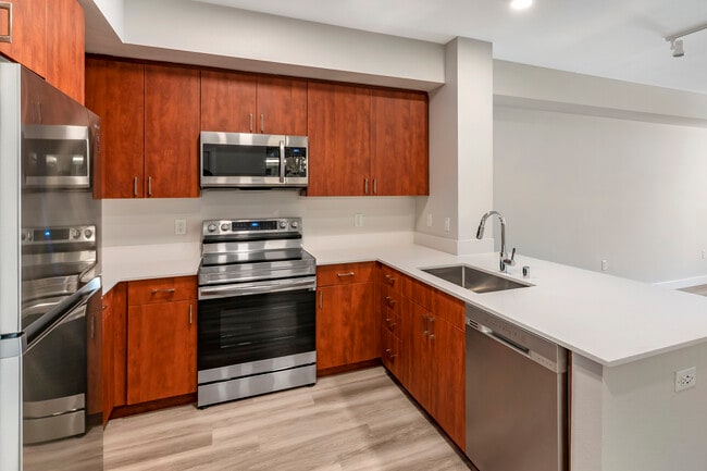 Renovated Package I kitchen with stainless steel appliances, white quartz countertops, cherry cabinetry, and hard surface flooring - Avalon Union City