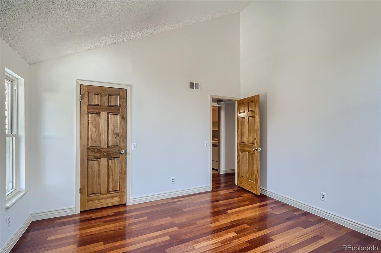 Primary bedroom with vaulted ceilings, closet door, window on the left and entrance door - 14282 E Tufts Pl