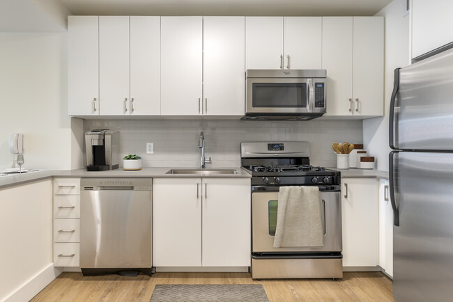 Renovated II North/South kitchen with stainless steel appliances, grey quartz countertops, white lacquer cabinetry, white tile backsplash, and hard surface flooring - Avalon Clinton