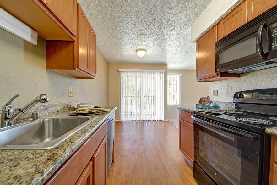 A kitchen with granite countertops, cabinet storage, and sleek black appliances with a view into the dining area - Avalon Springs