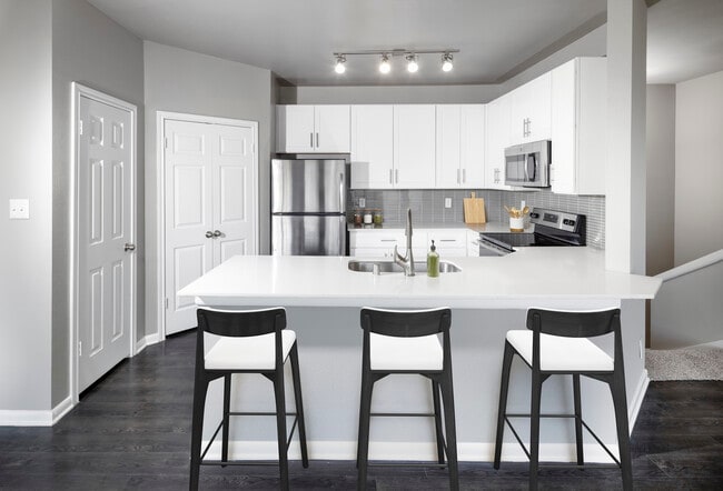 Classic Package II kitchen with stainless steel appliance, white quartz countertop, tile backsplash, white cabinetry, and hard-surface flooring - Avalon Addison