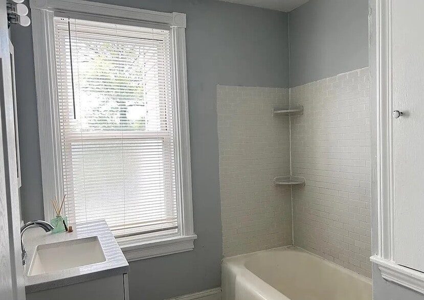 Updated bathroom with a full-size tub and shower, modern vanity, and classic tile surround. - 453 Lancaster Ave