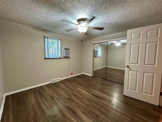 Bright room with elegant wood flooring, mirrored closet doors, and a modern ceiling fan, offering a comfortable and stylish living space. - Boardwalk Apartments