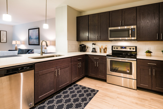 Gorgeous kitchen with shaker style cabinets, side by side stainless refrigerator, quartz countertops farmhouse sink and pendant lighting - The Haven at Indigo Square