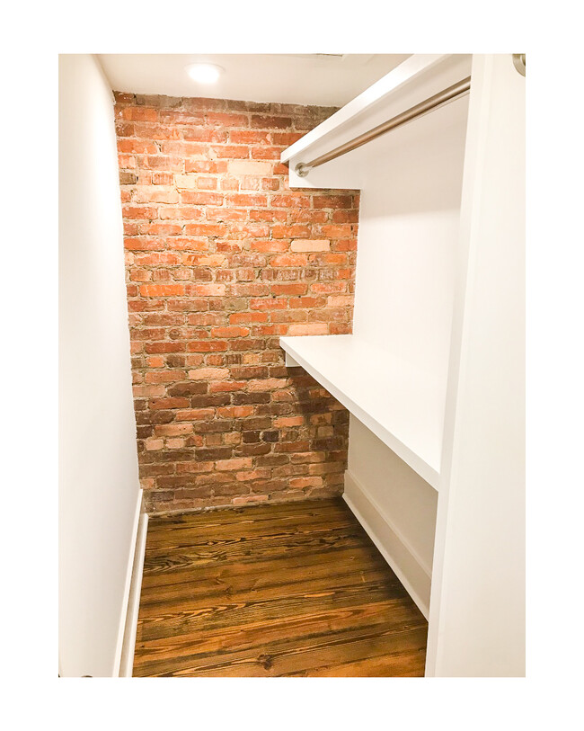 Spacious walk in closet with built-in shelves and hanging rods, exposed brick wall. - 18 W State St