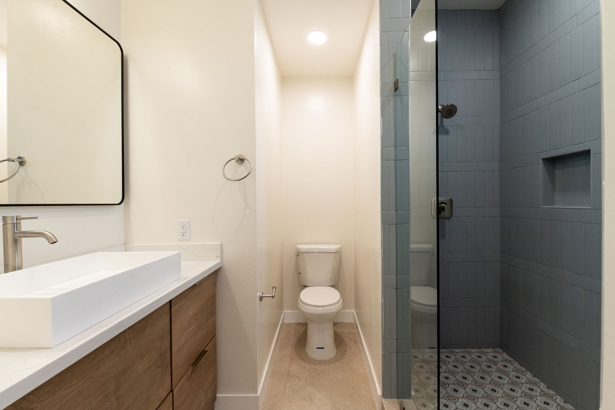Primary bath w/ floor to ceiling light blue porcelain tile, European style vanity w/ quartz counter - 4774 Bancroft St