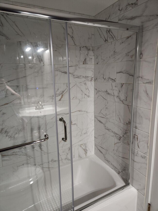 Guest bathroom bathtub with calacatta gold ceramic tile surround and glass-sliding door. - 434 Clinton Pl