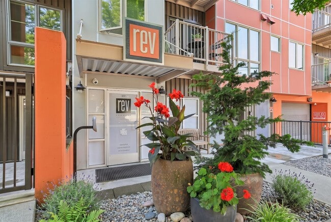 Street-level entrance to REV Fremont featuring secure access, colorful modern facade accents, and landscaped planters. - REV Fremont