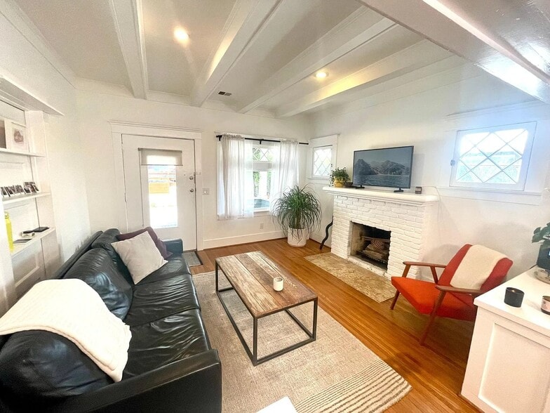Charming living room with original hardwood floors, exposed beams, and a decorative fireplace. - 6000 Carlton Way