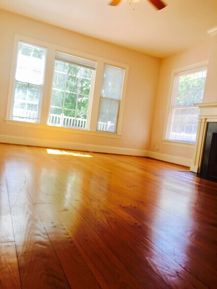 Living area with high ceilings, hardwood floors, and bright windows facing greenery. - 1937 Fairfield Dr