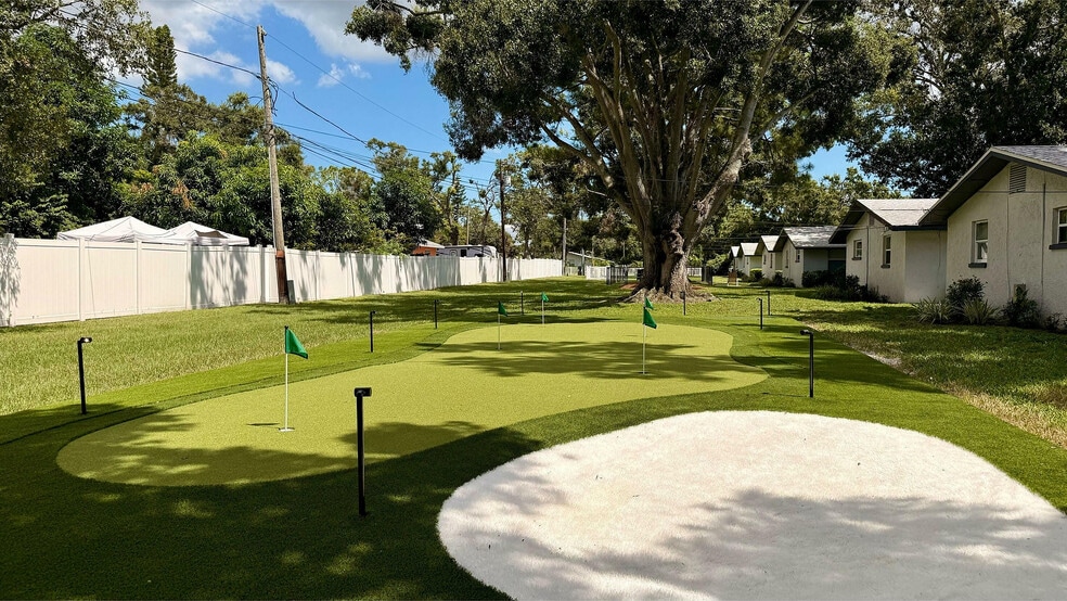 Charming outdoor view with a well-maintained putting green surrounded by lush greenery and quaint cottages under a clear blue sky. - Waterside Village