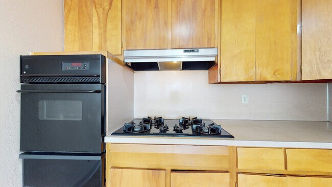 Step into a sleek kitchen featuring elegant wooden cabinets and a top-of-the-line gas stovetop. - Harmony Apartments