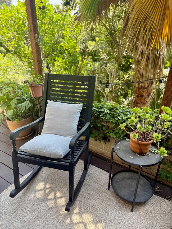 Outdoor deck furnished with a wooden rocking chair, potted succulents, and ambient lighting. - 1672 Rotary Dr