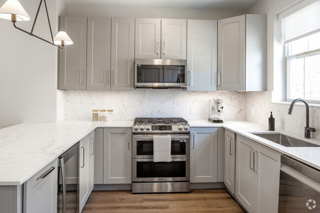 Signature Collection kitchen with stainless steel appliances, white quartz countertop, grey cabinetry, white quartz backsplash, and hard surface flooring - Avalon Princeton Circle