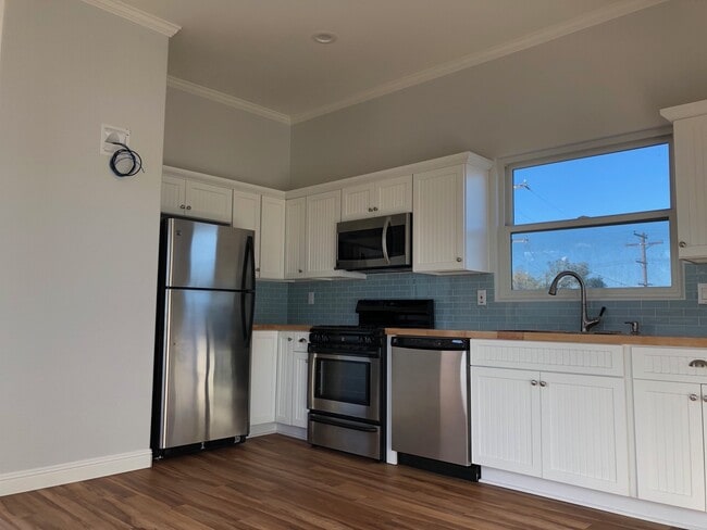 Galley kitchen with full-size appliances. Fridge/freezer, 4-burner stove plus oven, and dishwasher. Wiring on wall is for a TV mount. - 4470 Swift Ave