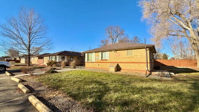 Charming brick ranch-style home with large front yard in a serene neighborhood setting, bathed in sunlight. - Flats at 16th