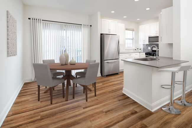 Kitchen and dining with white cabinetry, grey quartz countertops, grey tile backsplash, stainless steel appliances, and hard surface flooring - Avalon at the Hingham Shipyard