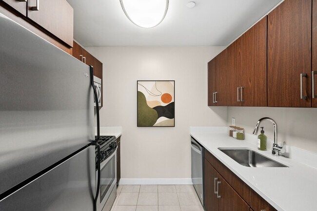 Kitchen with espresso cabinetry, white quartz countertops, stainless steel appliances, and hard surface flooring - Avalon West Chelsea