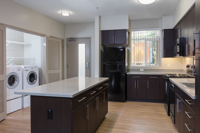 Classic Package I kitchen with black appliances, grey speckled granite countertops, espresso cabinetry, and hard surface flooring - Avalon Ocean Avenue